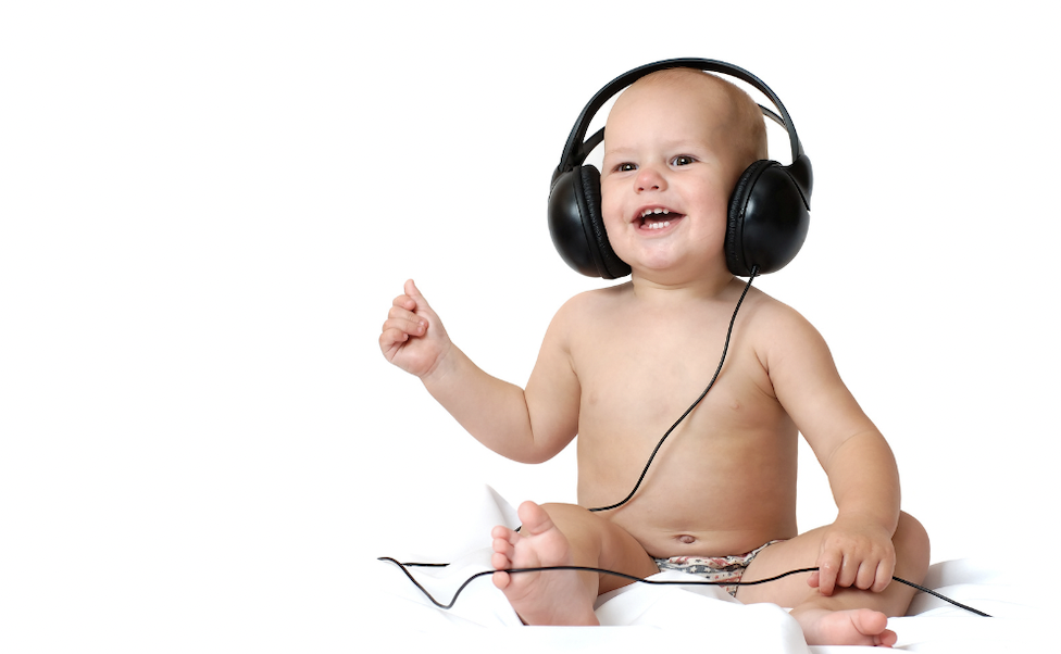 Caucasian baby sitting up and smiling. The baby is wearing only a nappy and has big black headphones on